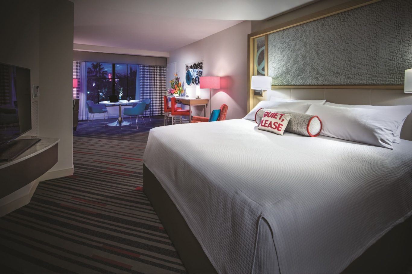 Modern hotel room featuring a large bed, colourful decor, and a view of the city.