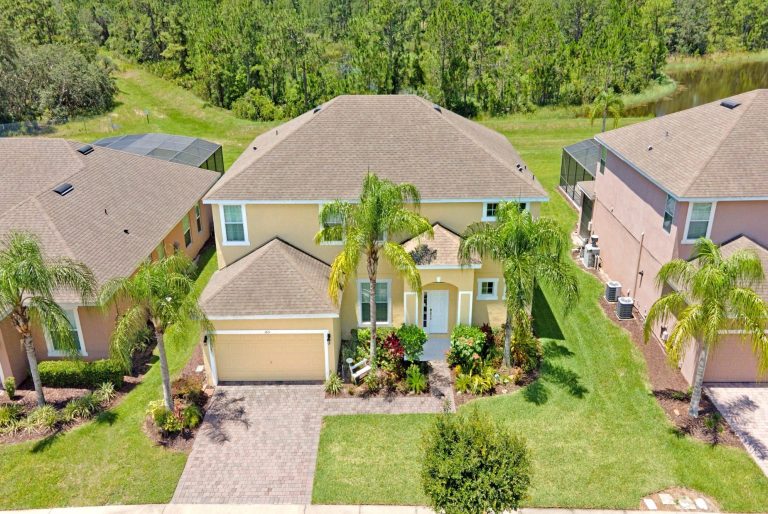 Aerial view of a yellow house surrounded by palm trees and manicured lawns.