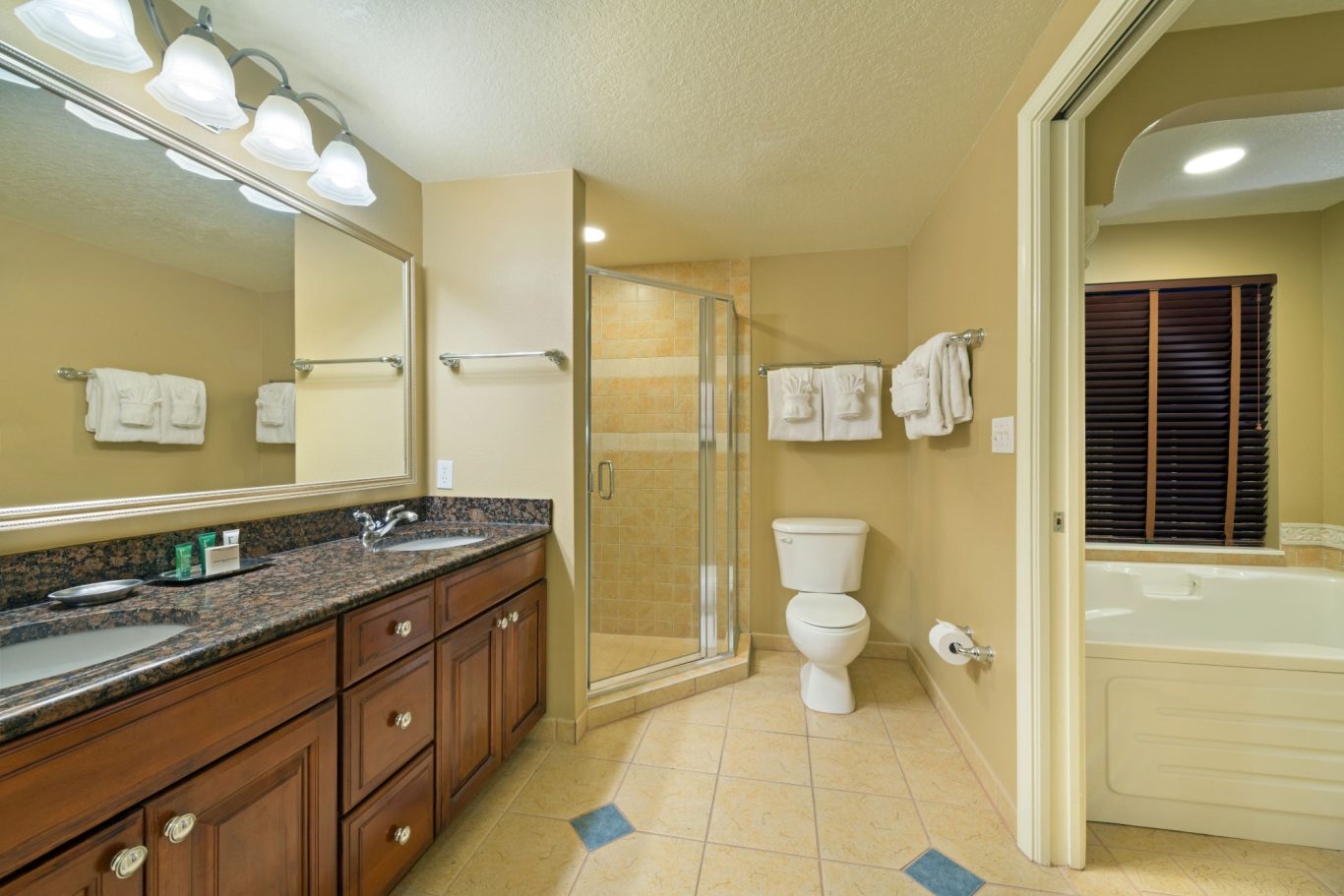 Modern bathroom featuring a shower, toilet, sink, and bathtub. Warm tones and bright lighting.