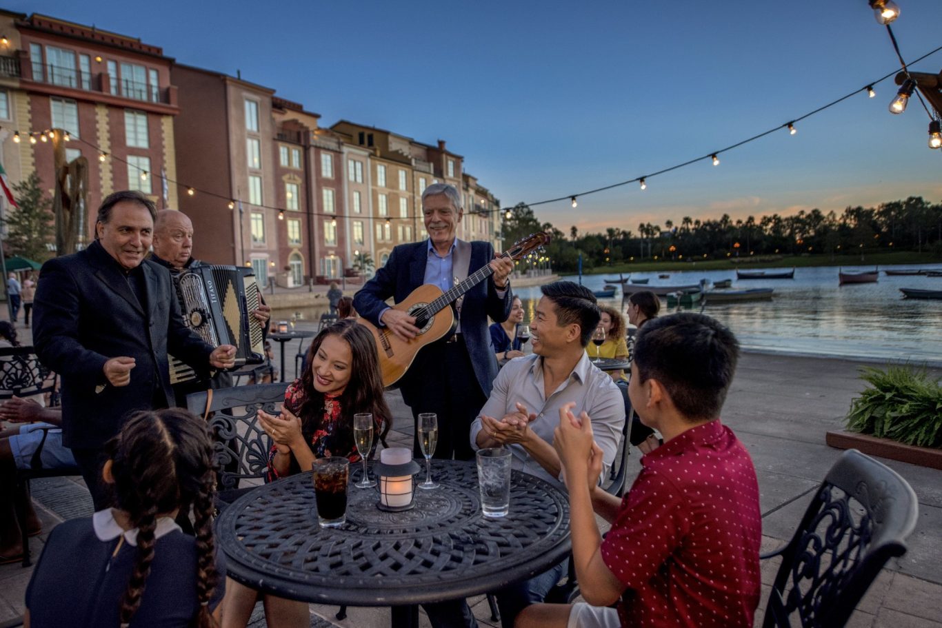 A group enjoying an outdoor gathering with music, drinks, and a waterfront view at sunset.