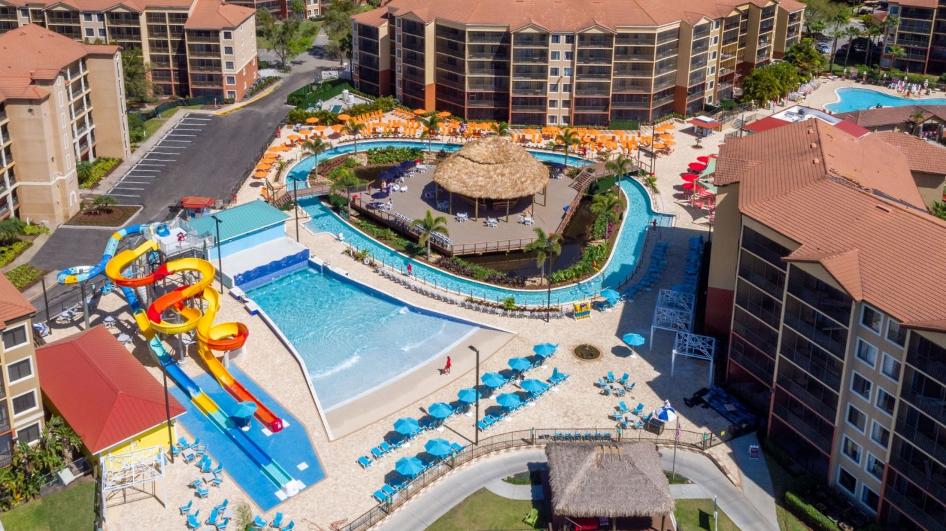 Aerial view of a resort pool with slides, sun loungers, and surrounding buildings.