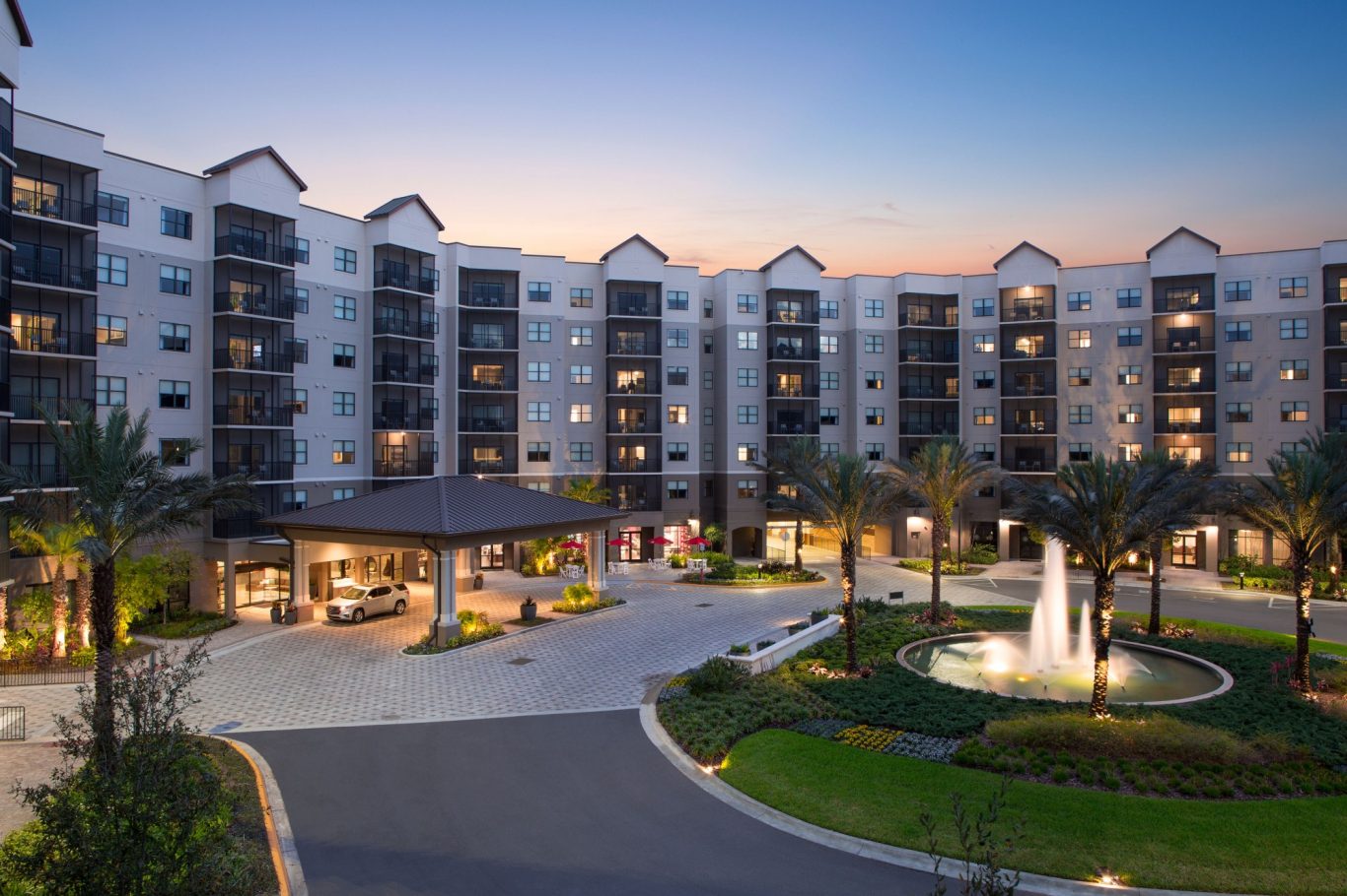 Modern hotel exterior with palm trees and fountain at sunset.