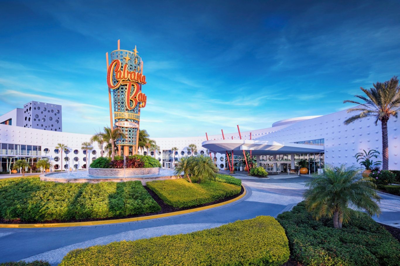 Bright blue sky over a modern building with a prominent sign and palm trees.