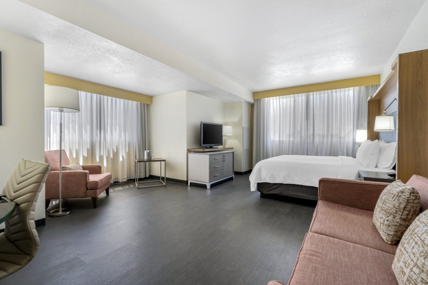 Modern hotel room with a bed, seating area, TV, and large windows.