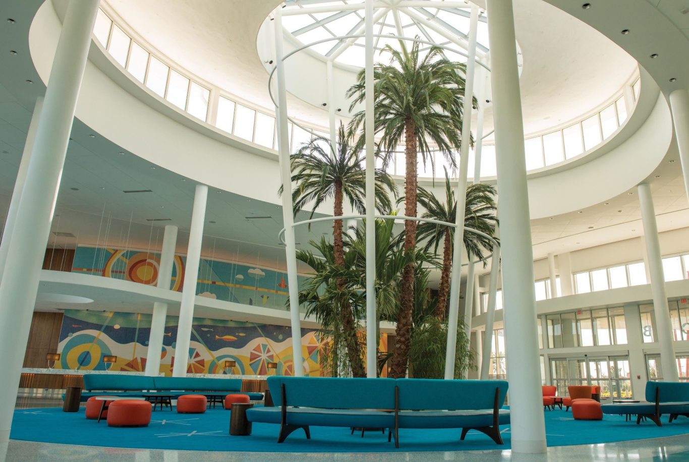 Modern interior space with tall palm trees, colourful murals, and blue seating.