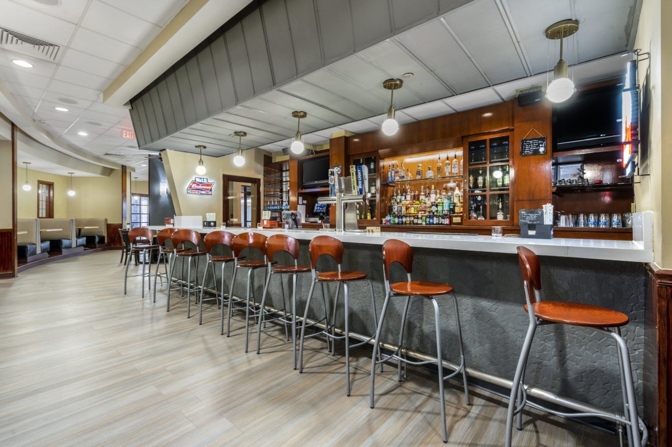 A modern bar with high stools, wooden counter, and shelves of drinks in a spacious setting.