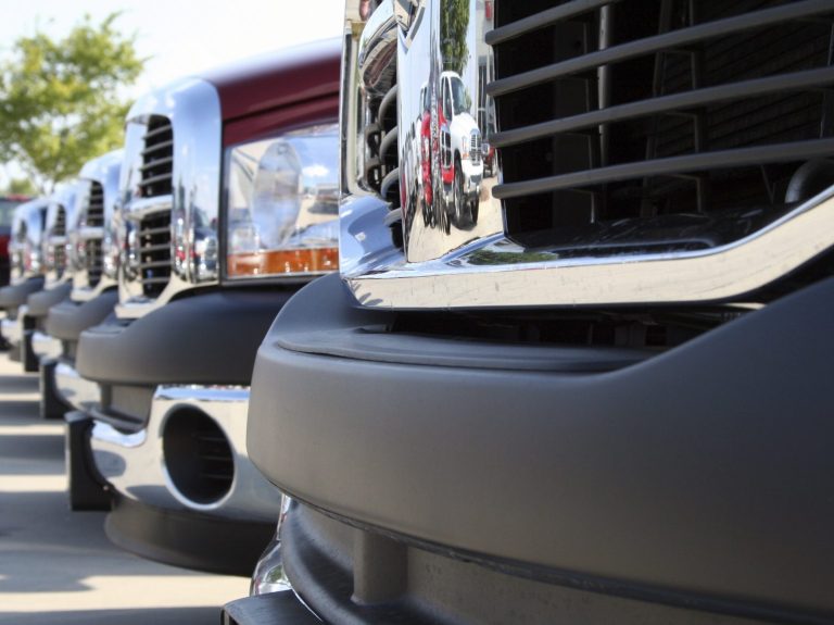 Close-up of the front grilles and bumpers of several trucks lined up.