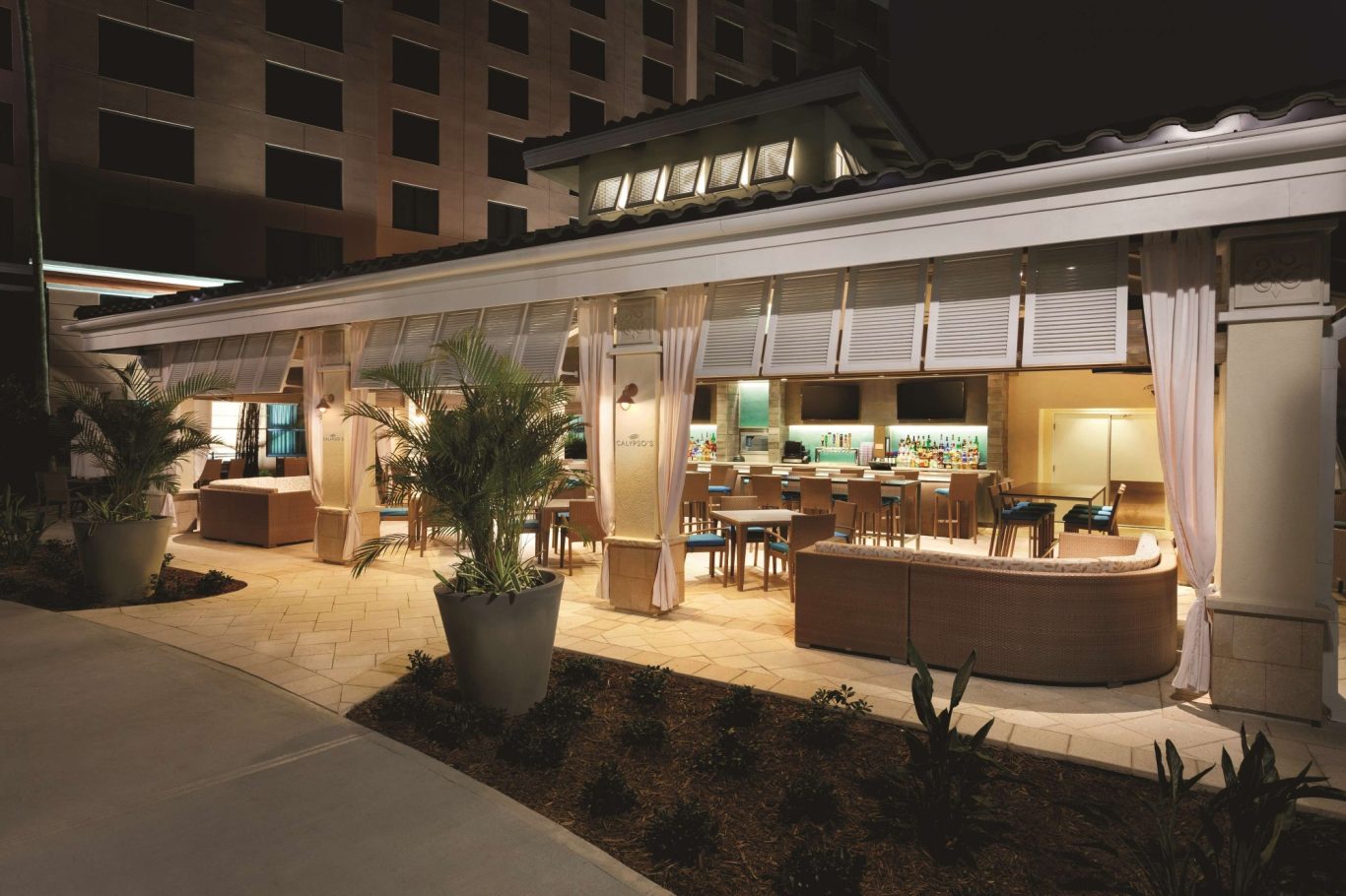 Exterior of a restaurant at night with outdoor seating and decorative plants.