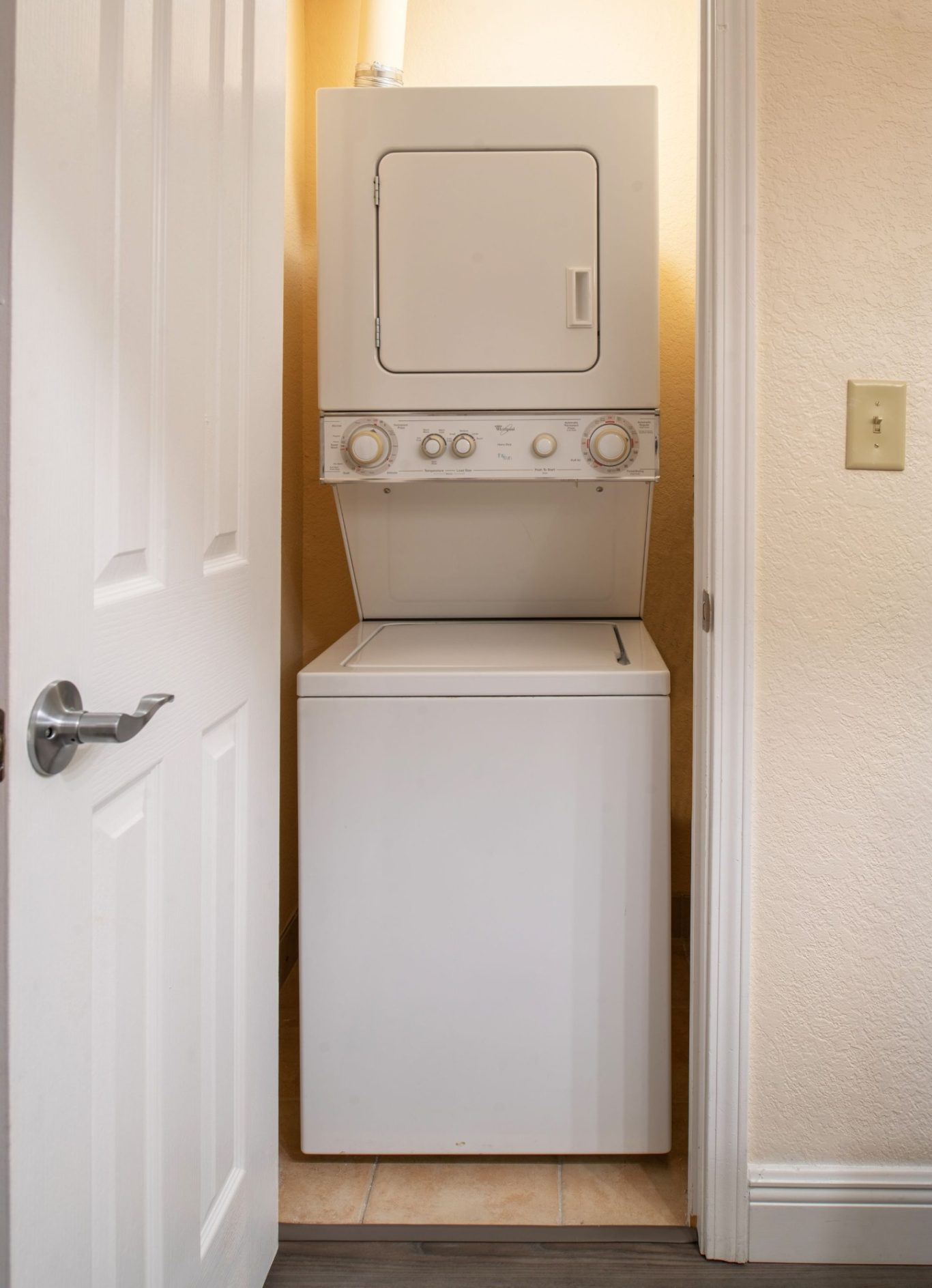 Stacked washer and dryer unit in a small laundry space with light-coloured walls.