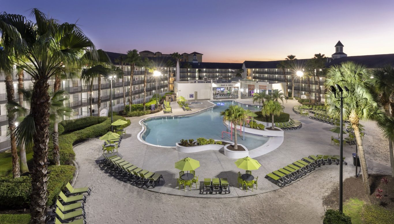 Hotel courtyard with a pool, palm trees, and lounge chairs at dusk.