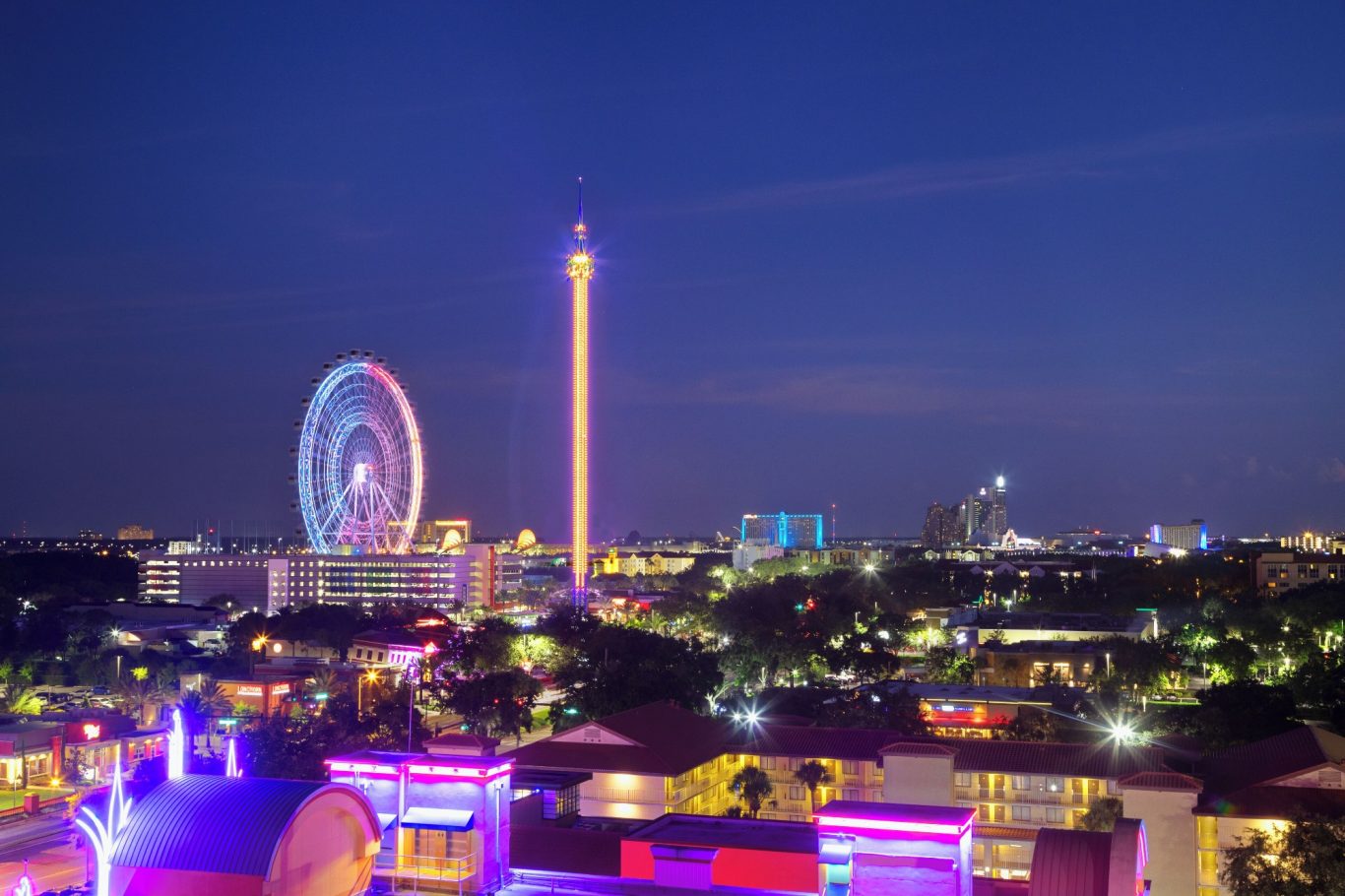 Night view of a city skyline featuring a ferris wheel and illuminated tower.