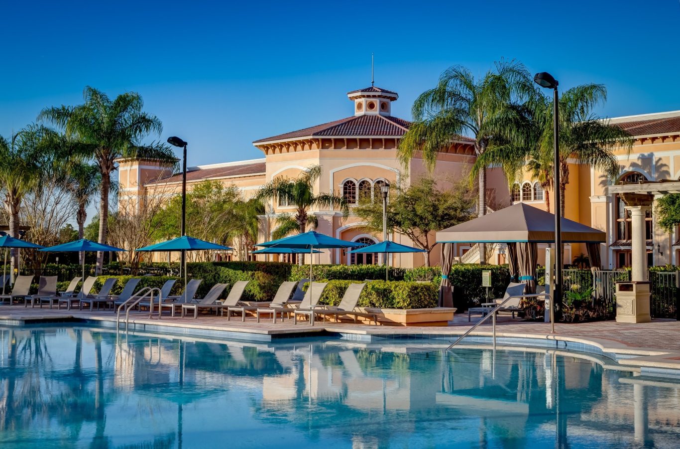 Sunny pool area with loungers and palm trees beside a stylish resort building.