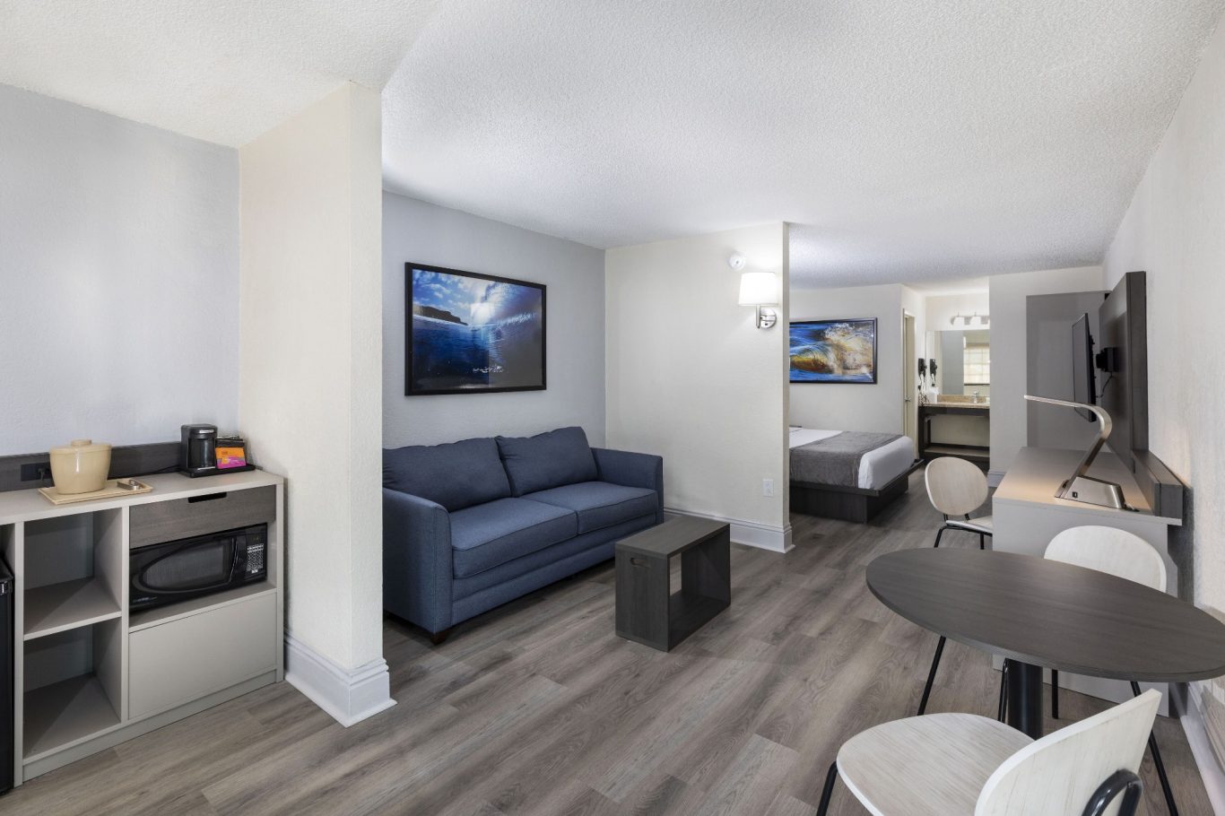 A modern hotel room featuring a seating area, kitchenette, and a double bed.