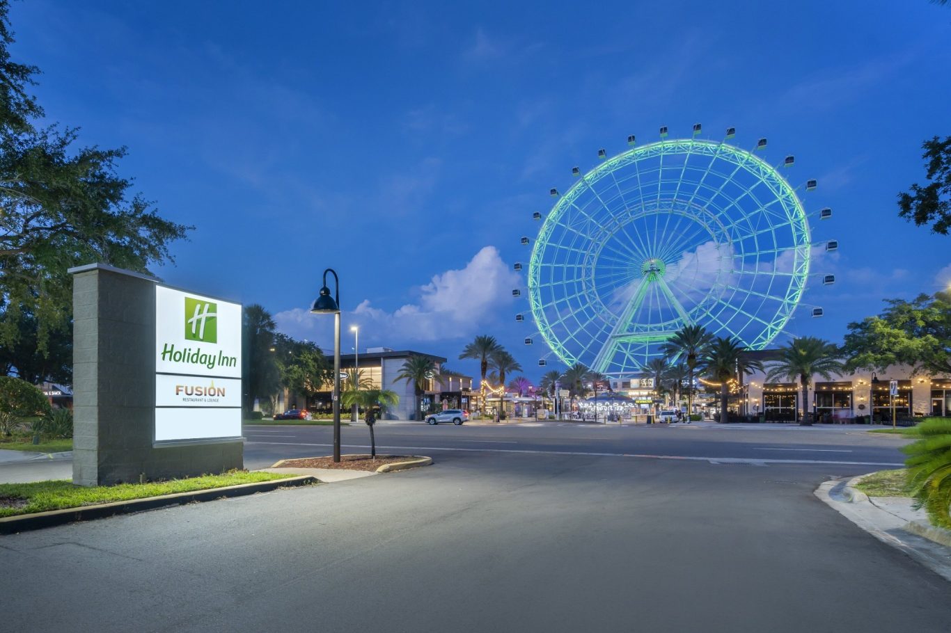 Holiday Inn entrance with a large green Ferris wheel in the background at dusk.