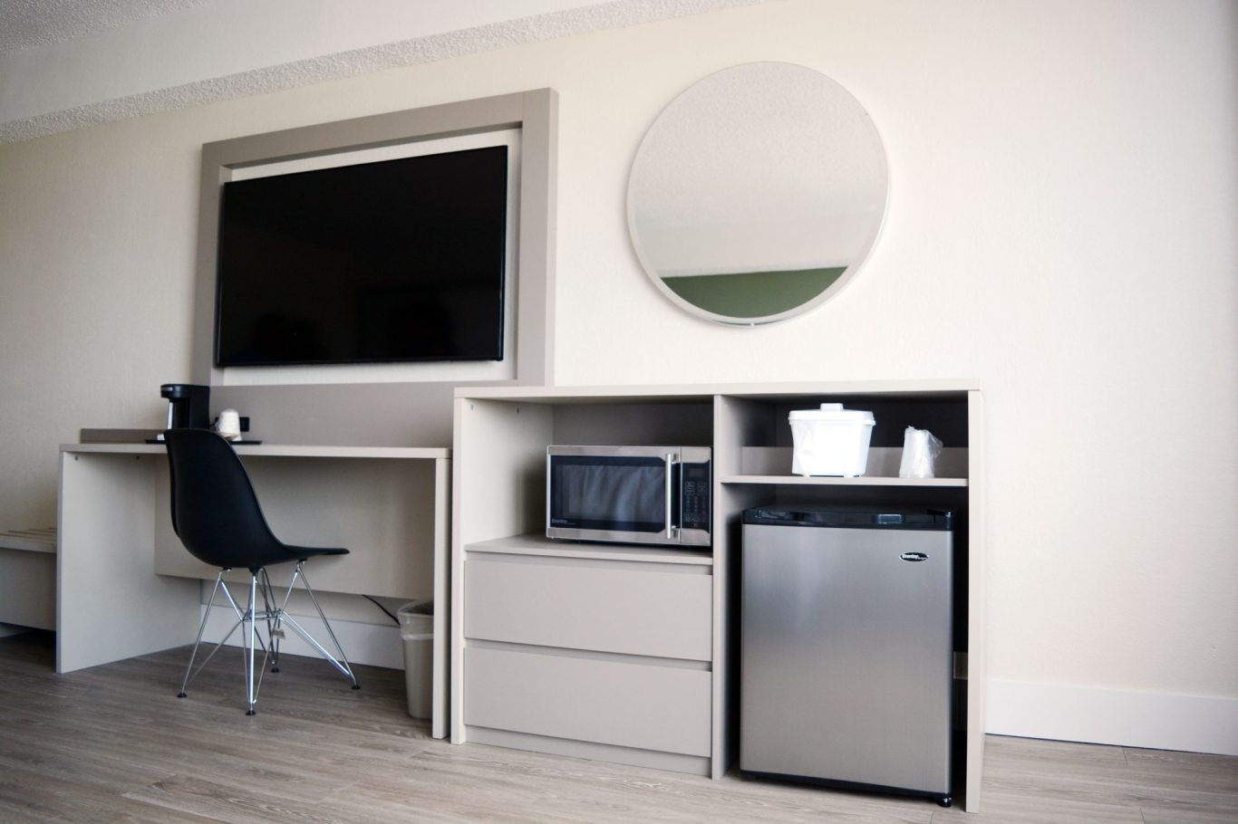 Modern hotel room workspace with a desk, TV, mirror, microwave, and mini-fridge.