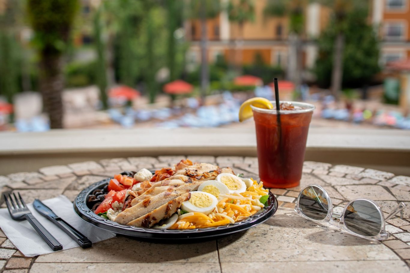 Grilled fish with lemon and garnish, alongside iced tea and sunglasses on a table.