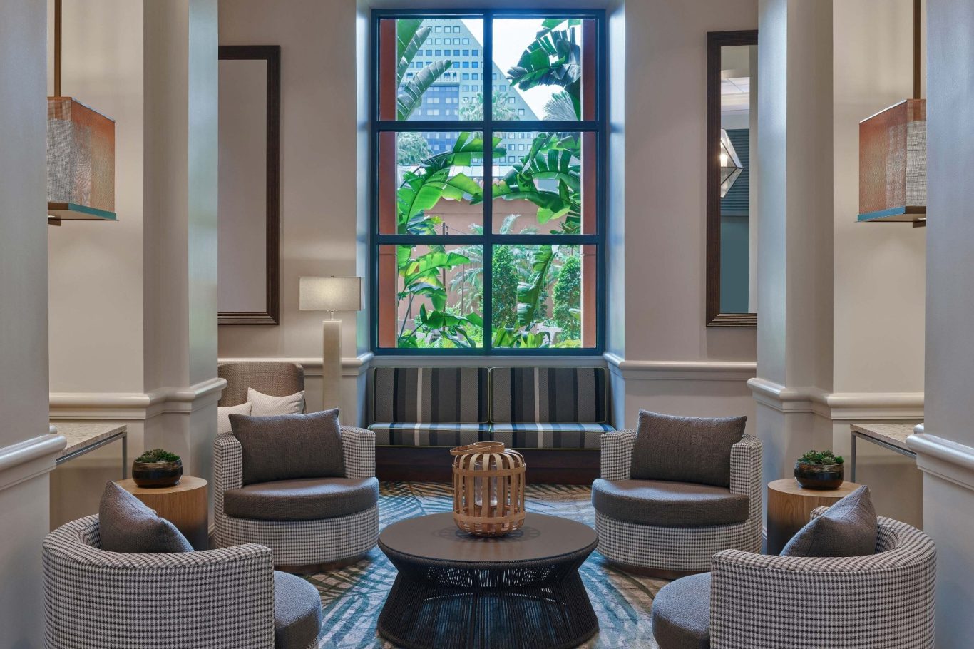 Elegant lounge with plush seating, a round table, and large windows showcasing greenery outside.