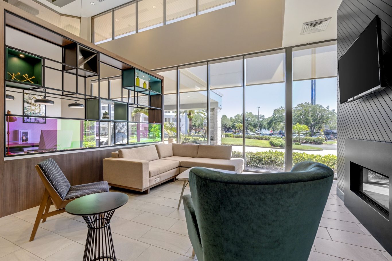 Modern lounge area with a beige sofa, green armchair, and large windows.
