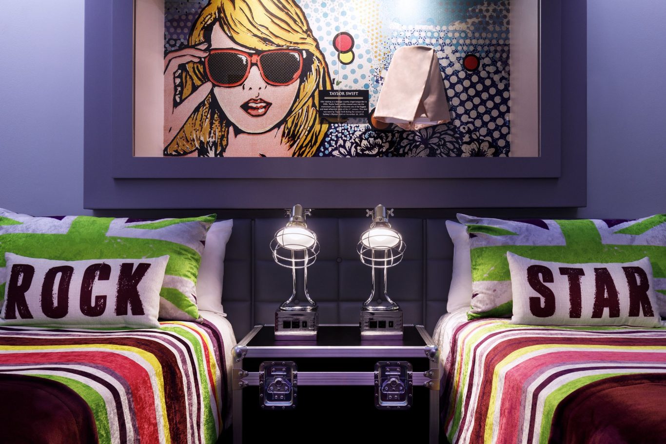A stylish bedroom featuring twin beds, vibrant cushions, and a pop art mural.