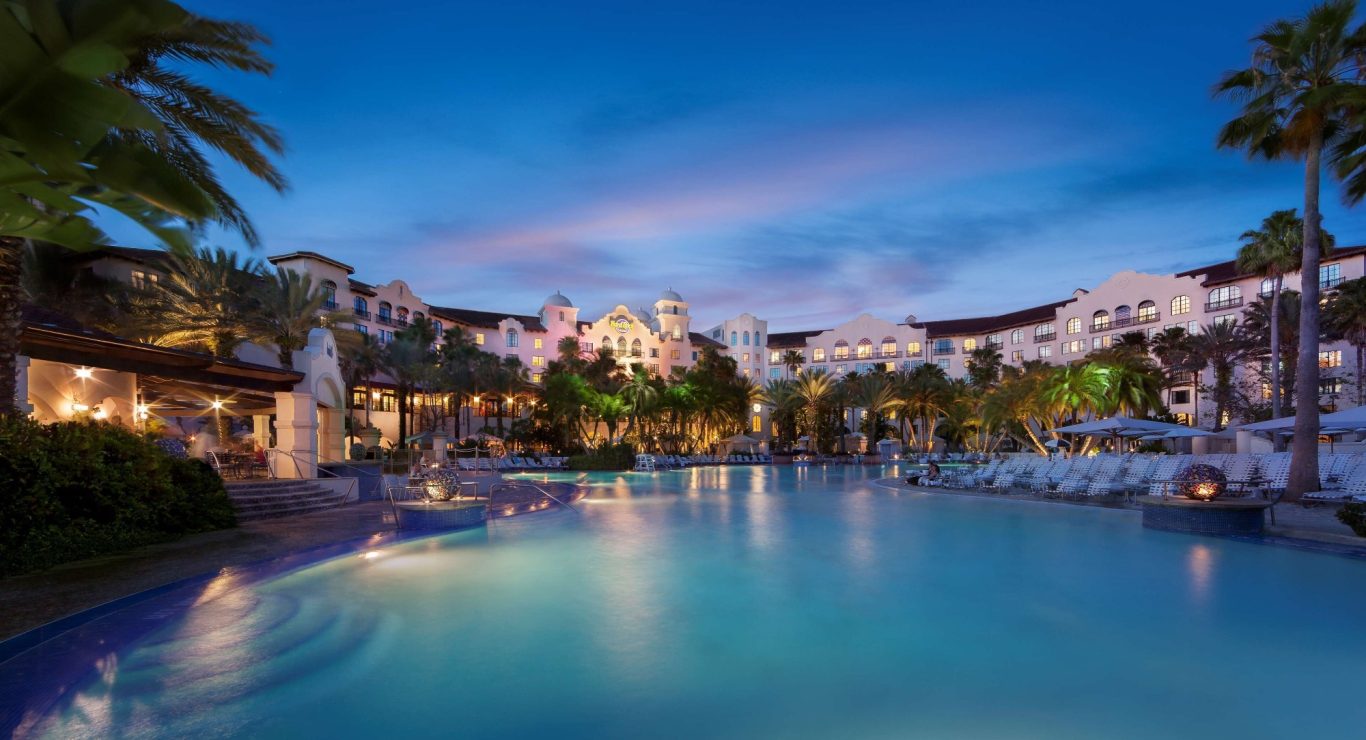 Luxury resort pool at twilight, surrounded by palm trees and illuminated buildings.