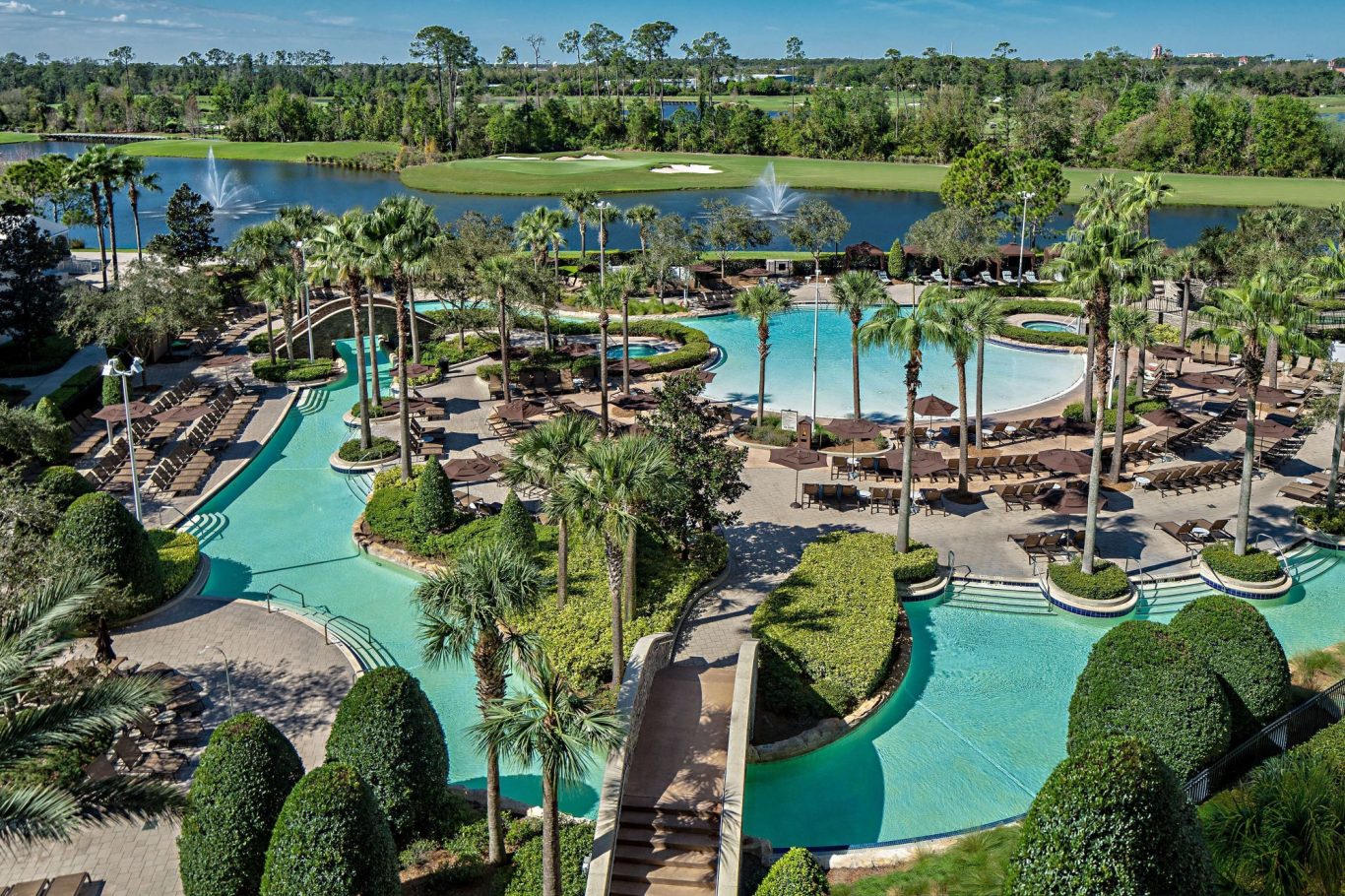 Aerial view of a landscaped resort pool area with palm trees and lounge chairs.