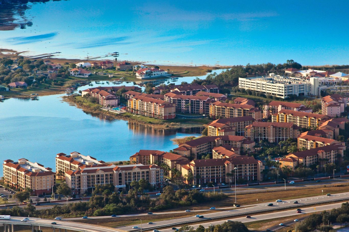 Aerial view of residential buildings alongside a lake with greenery and roads nearby.