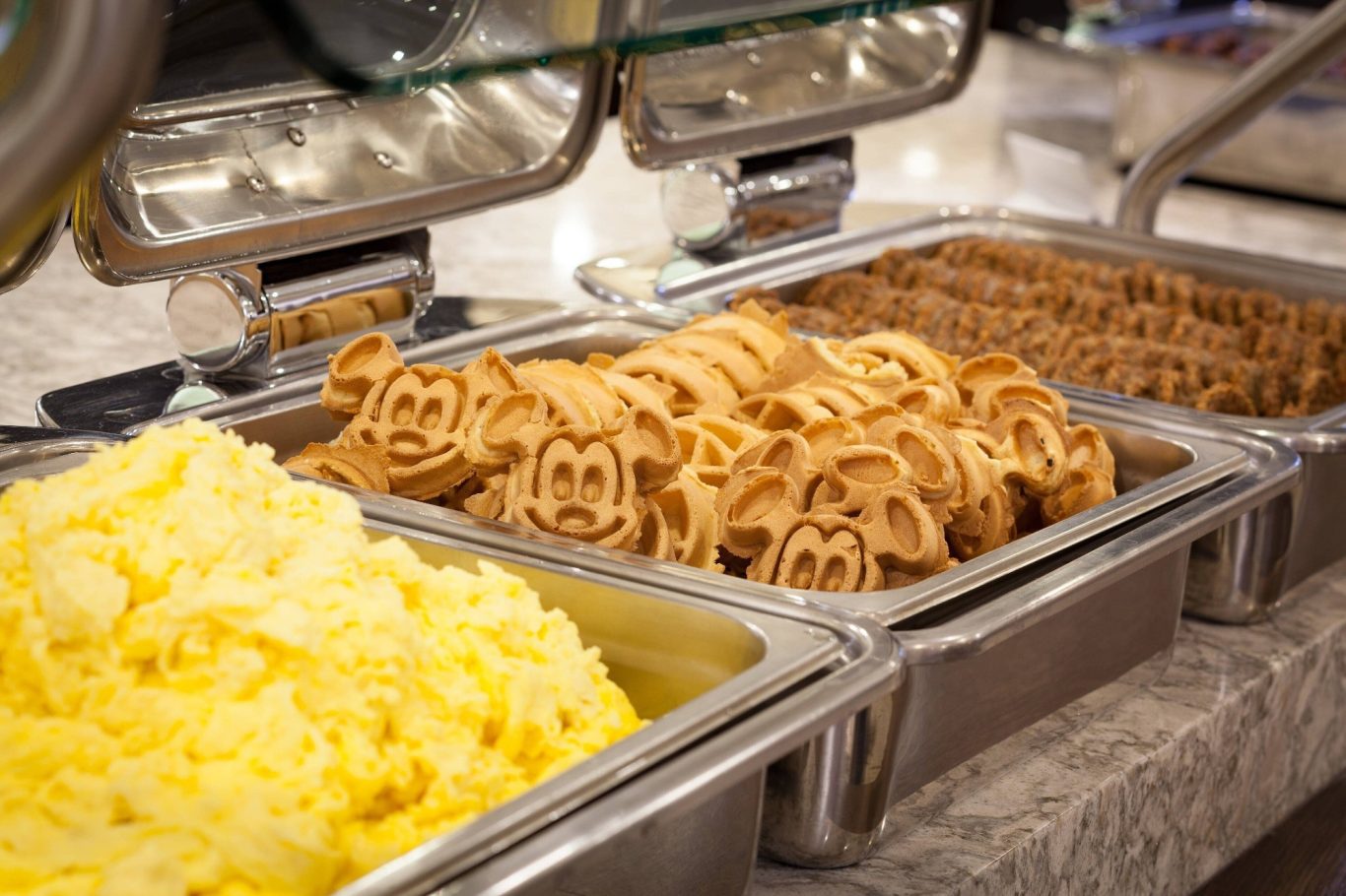 Yellow mashed potatoes, waffle shapes resembling pig faces, and sausages in buffet trays.