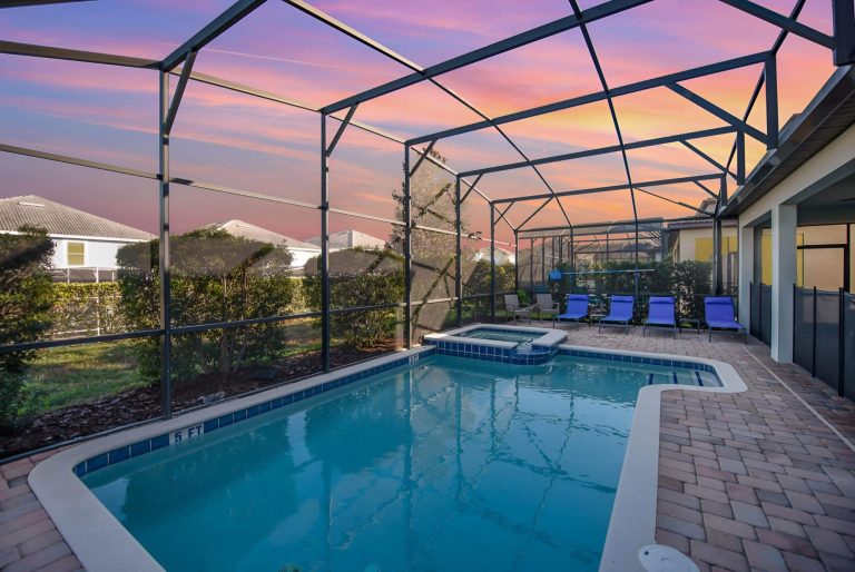 Swimming pool with lounge chairs, enclosed by a mesh screen, at sunset.