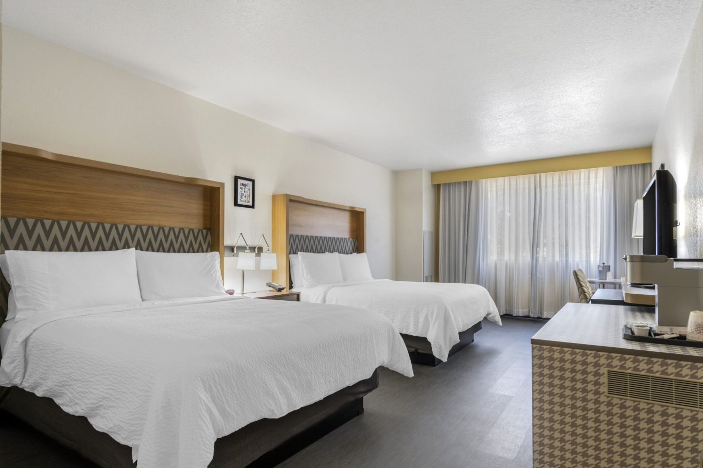 Hotel room with two beds, a TV, and a window with sheer curtains.