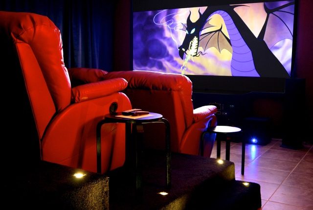 Red recliners in a home theatre with a dragon-themed projection on screen.