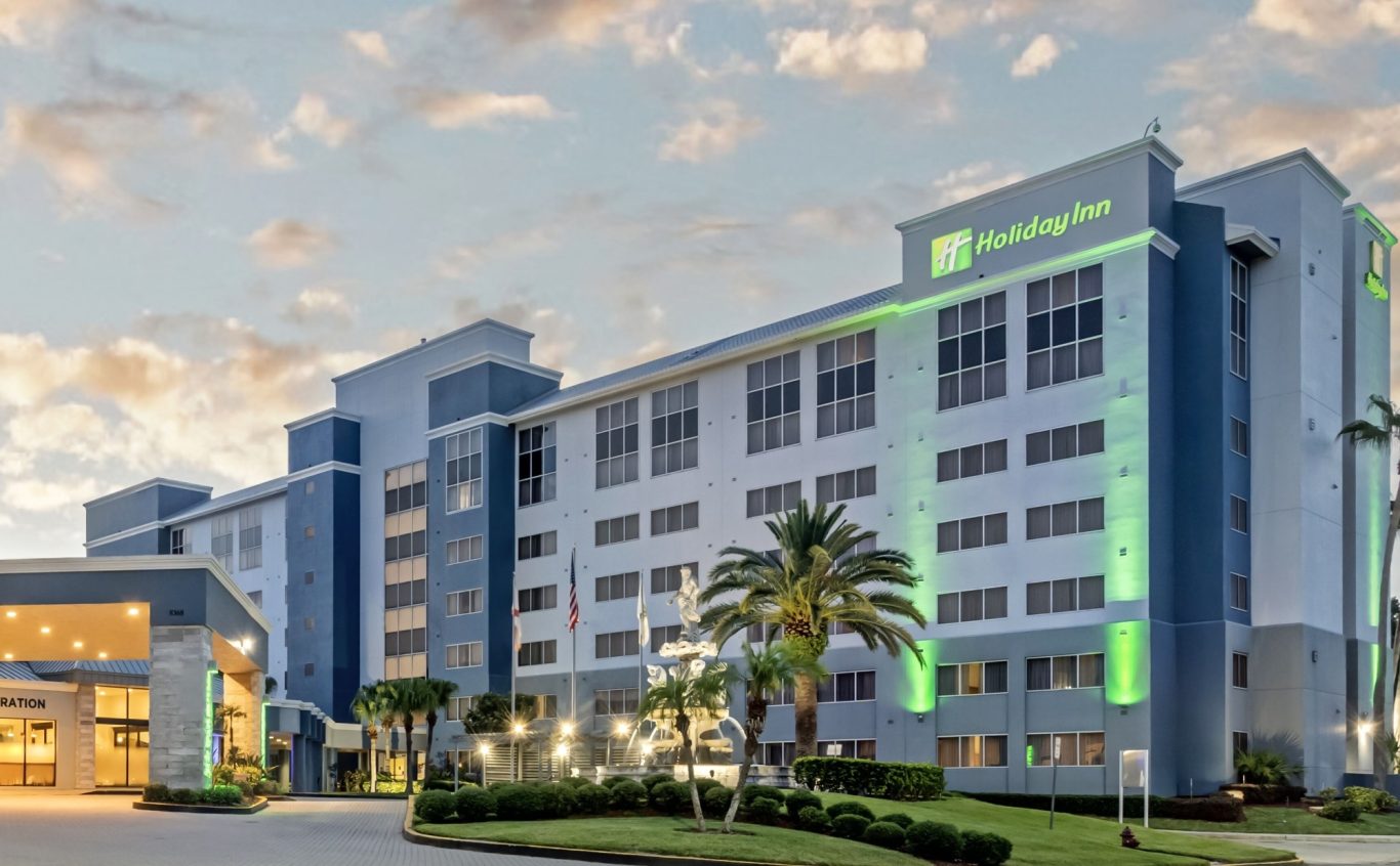 Modern hotel building with greenery and lights, set against a cloudy sky.
