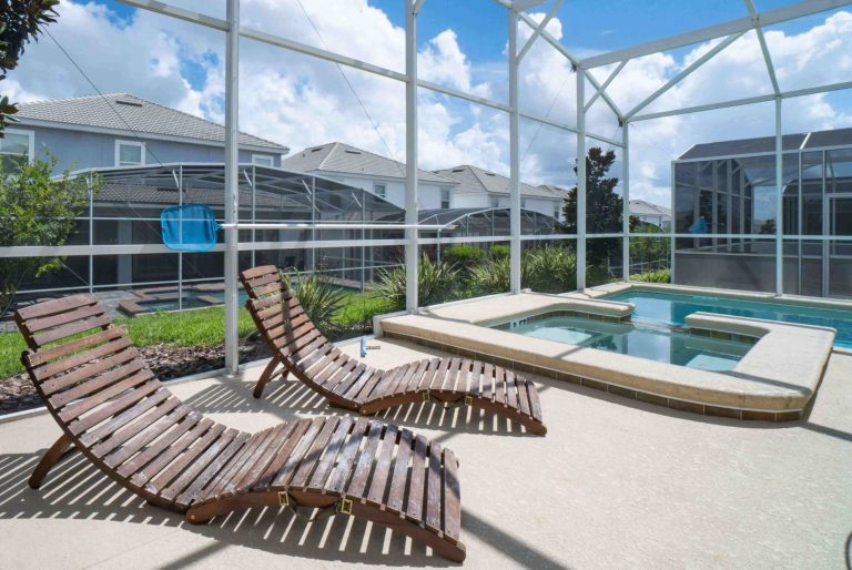 Two wooden loungers beside a hot tub on a patio surrounded by a screened enclosure.