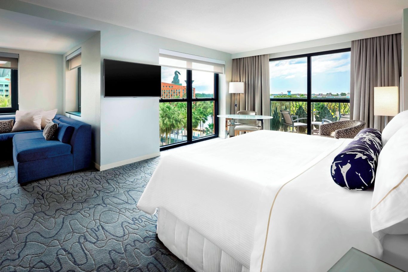 Modern hotel room with a king-size bed, large windows, and a seating area.