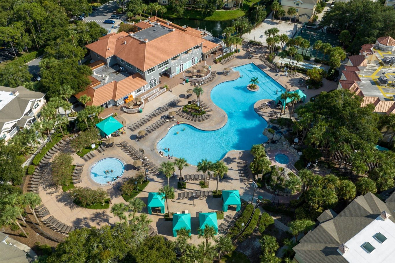 Aerial view of a large swimming pool area surrounded by greenery and lounge seating.