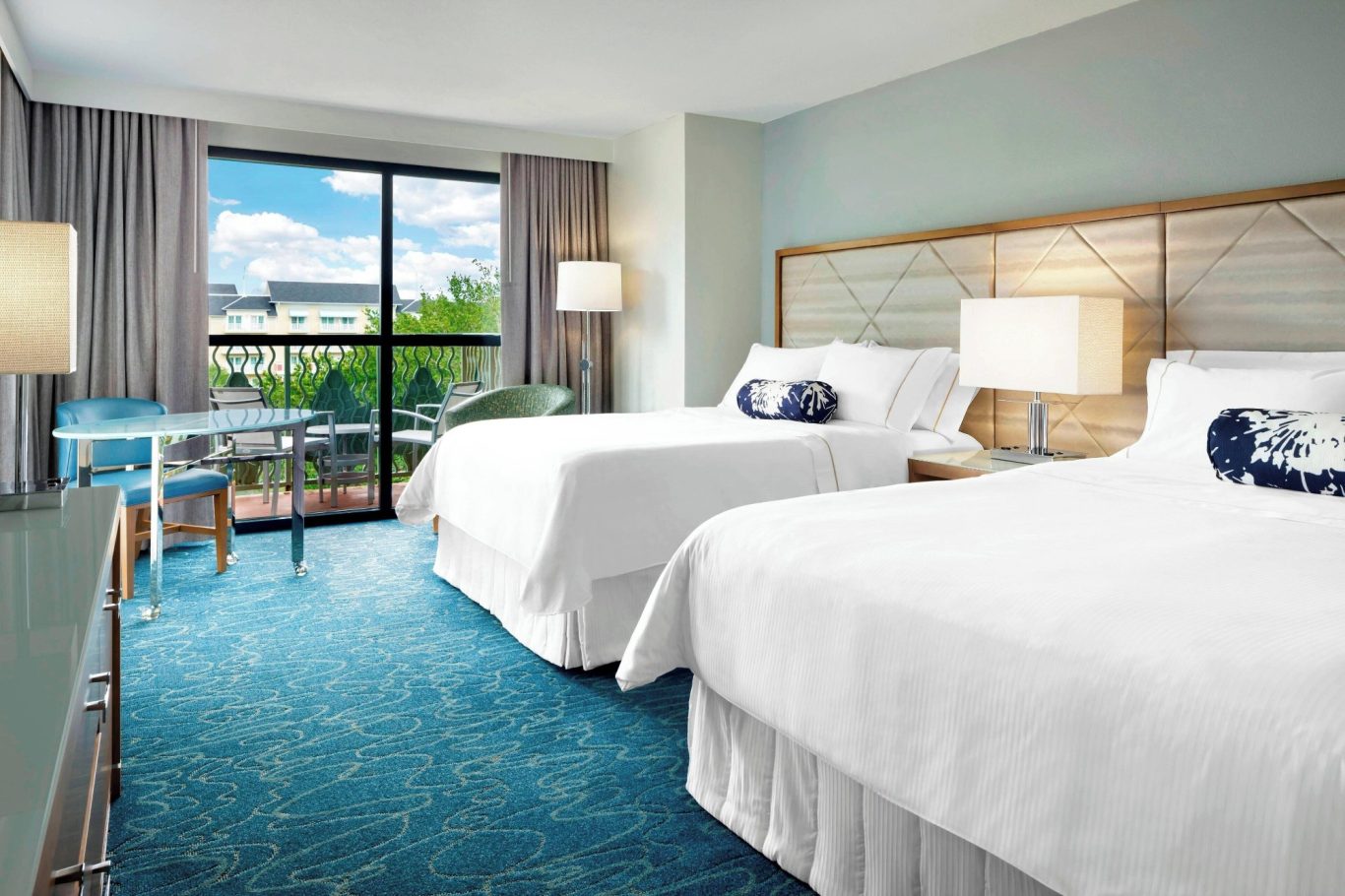 Modern hotel room with two beds, desk, and large window offering outside view.
