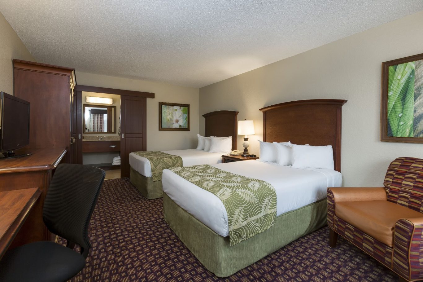Hotel room featuring two double beds, a desk, and a seating area with an armchair.