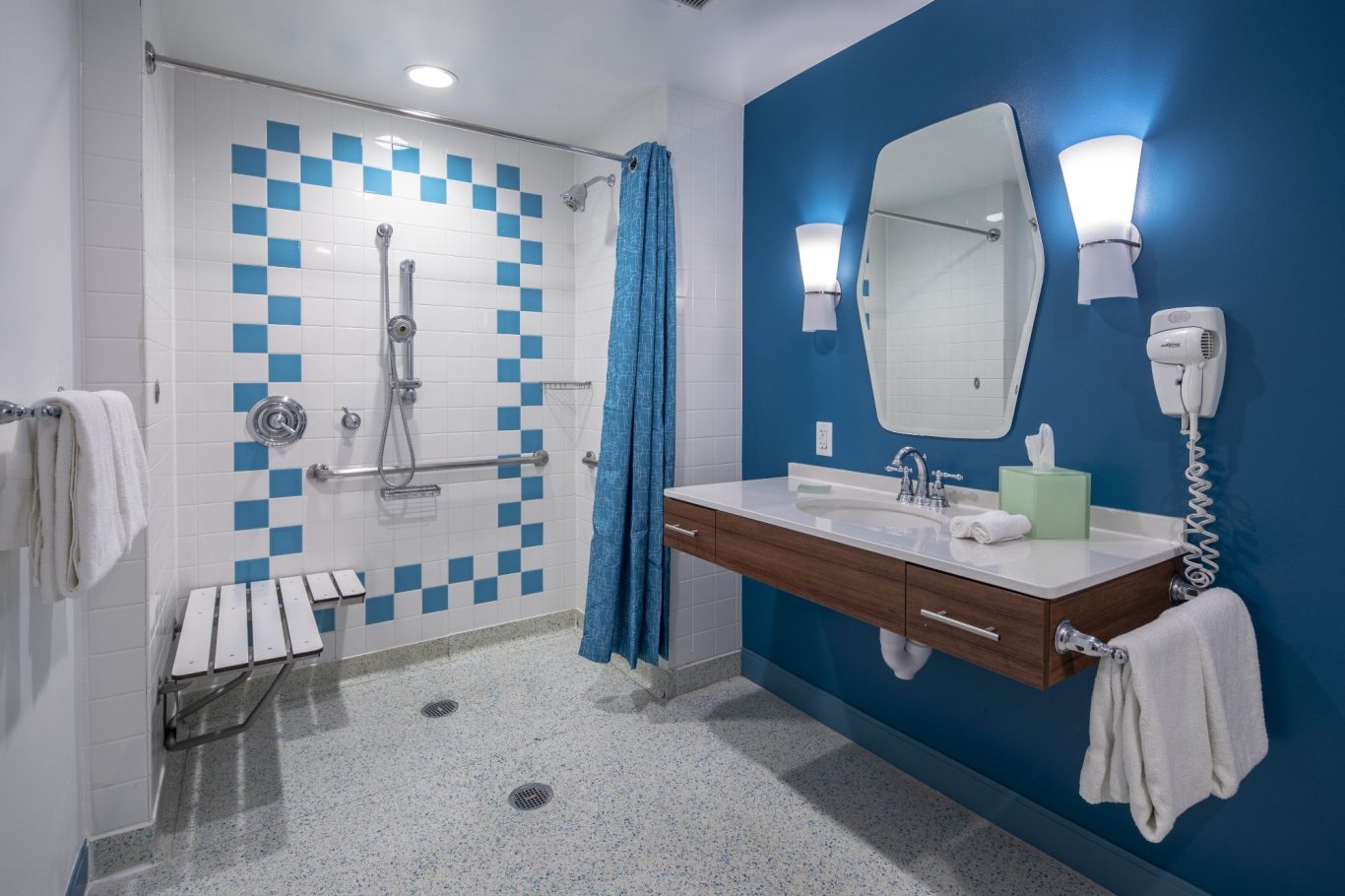 Modern bathroom with blue accents, walk-in shower, grab bars, and a large mirror.