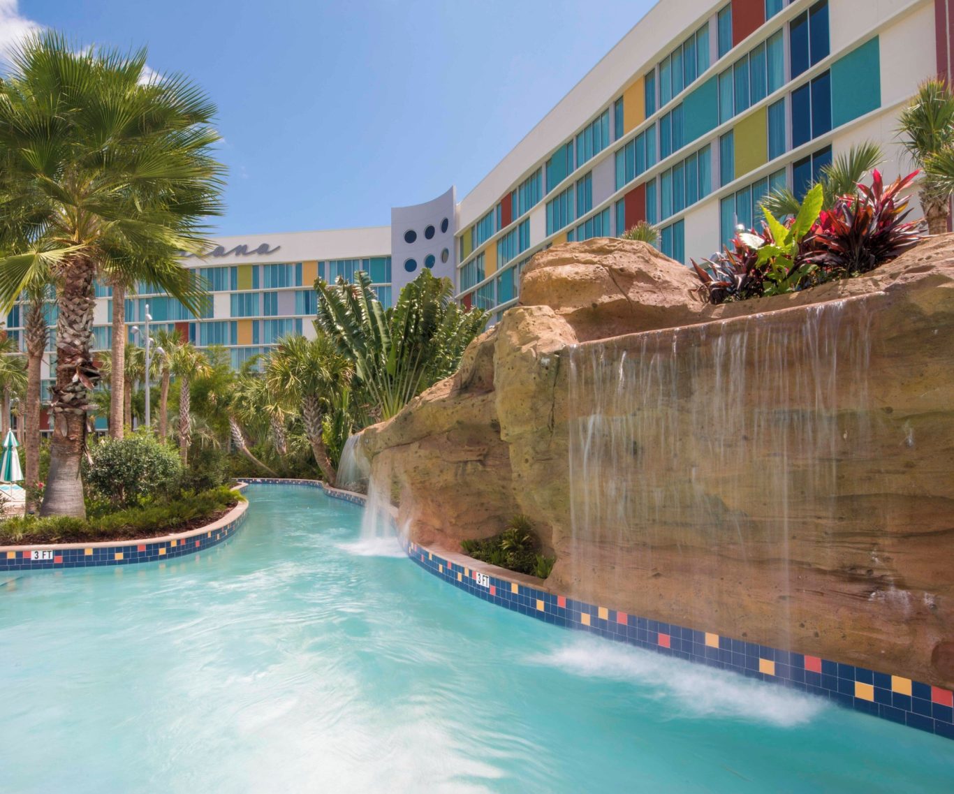 Tropical resort with a pool, waterfall, and colourful hotel facade in the background.
