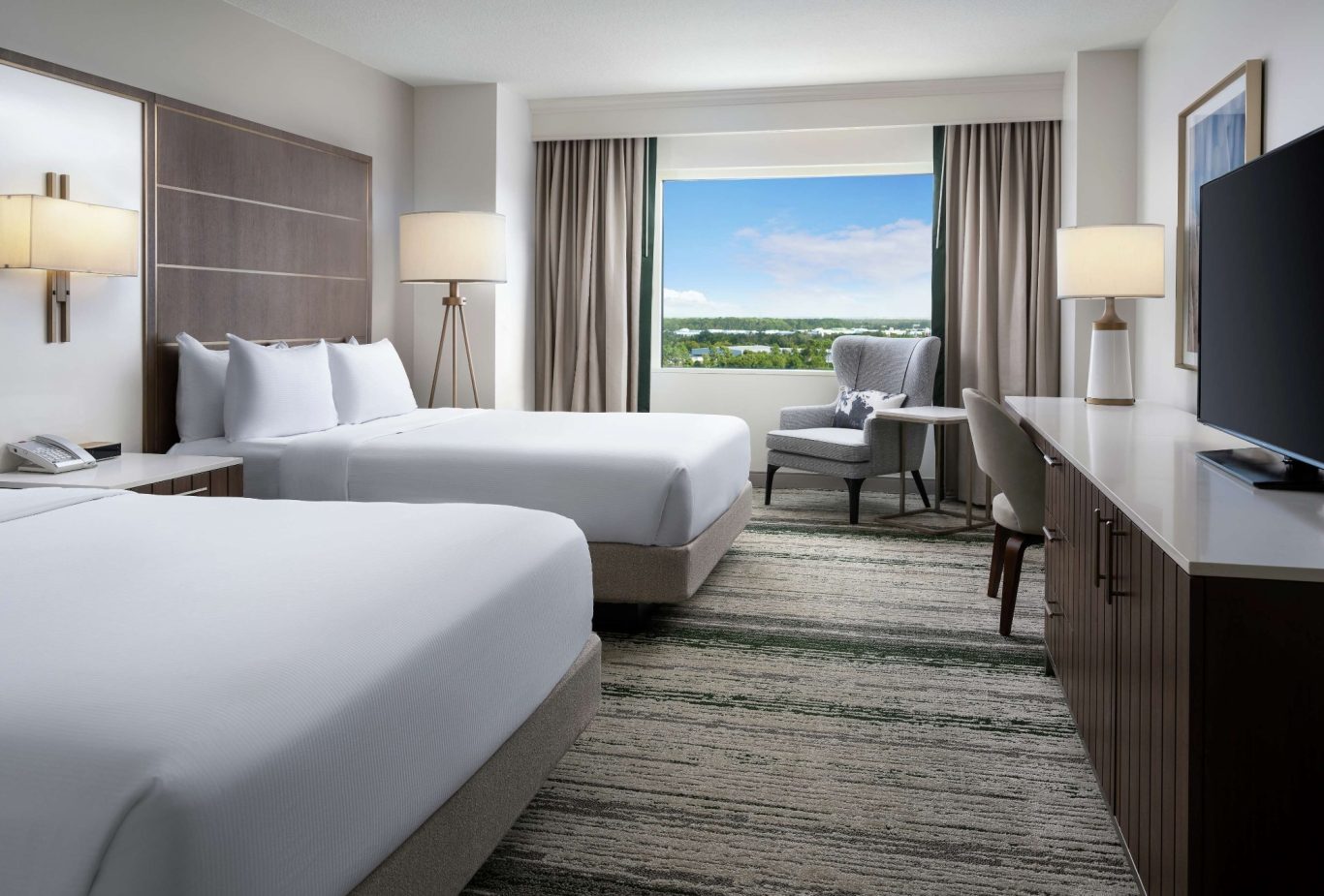 Modern hotel room with two beds, large windows, and a scenic view.