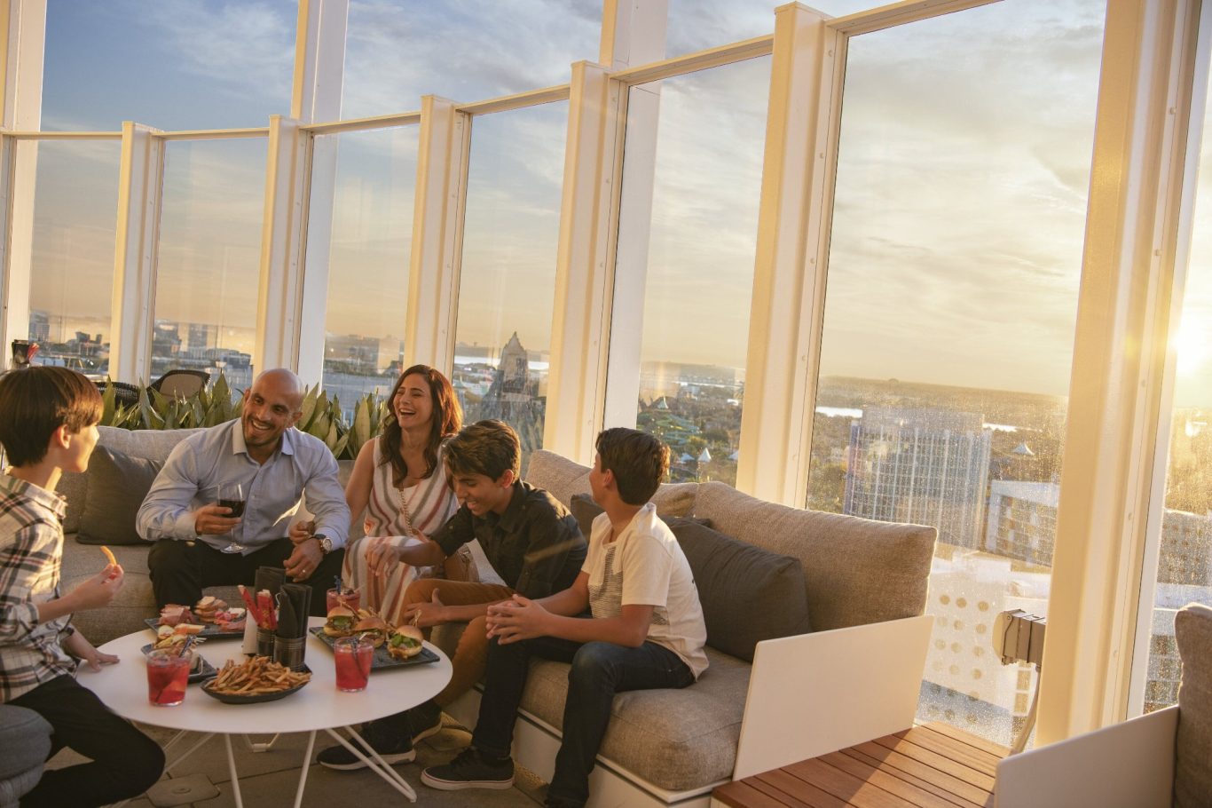 A group of people enjoying snacks and drinks with a city skyline at sunset in the background.