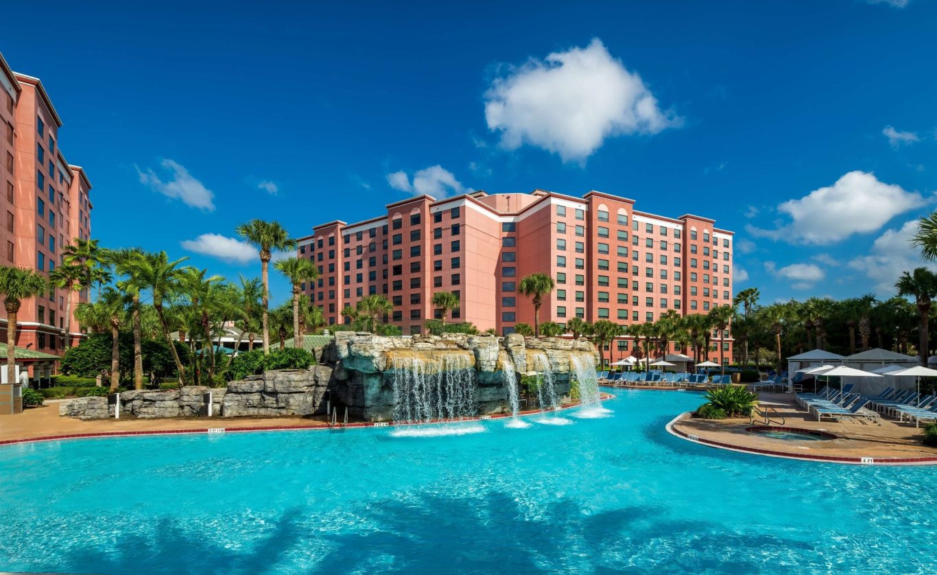 Tropical resort with a large pool, waterfall, palm trees, and a pink hotel.