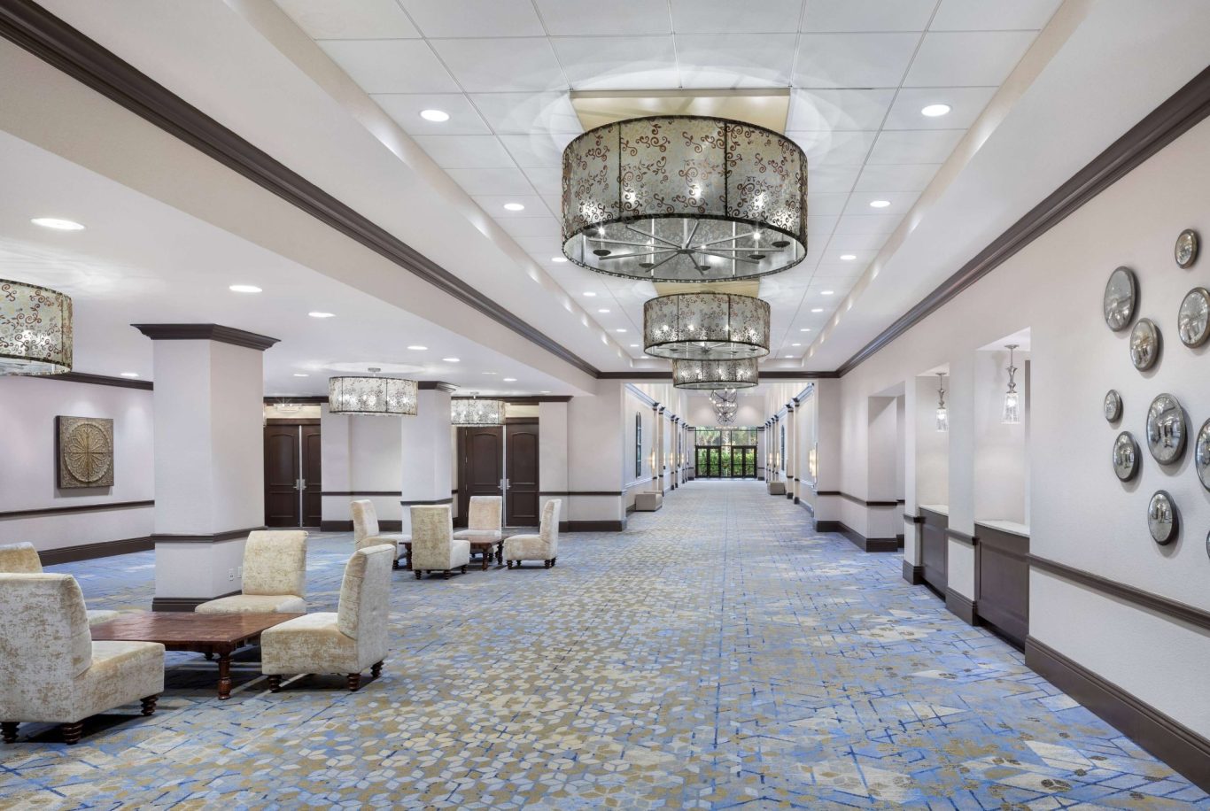 Spacious hotel corridor with chandeliers and seating areas.