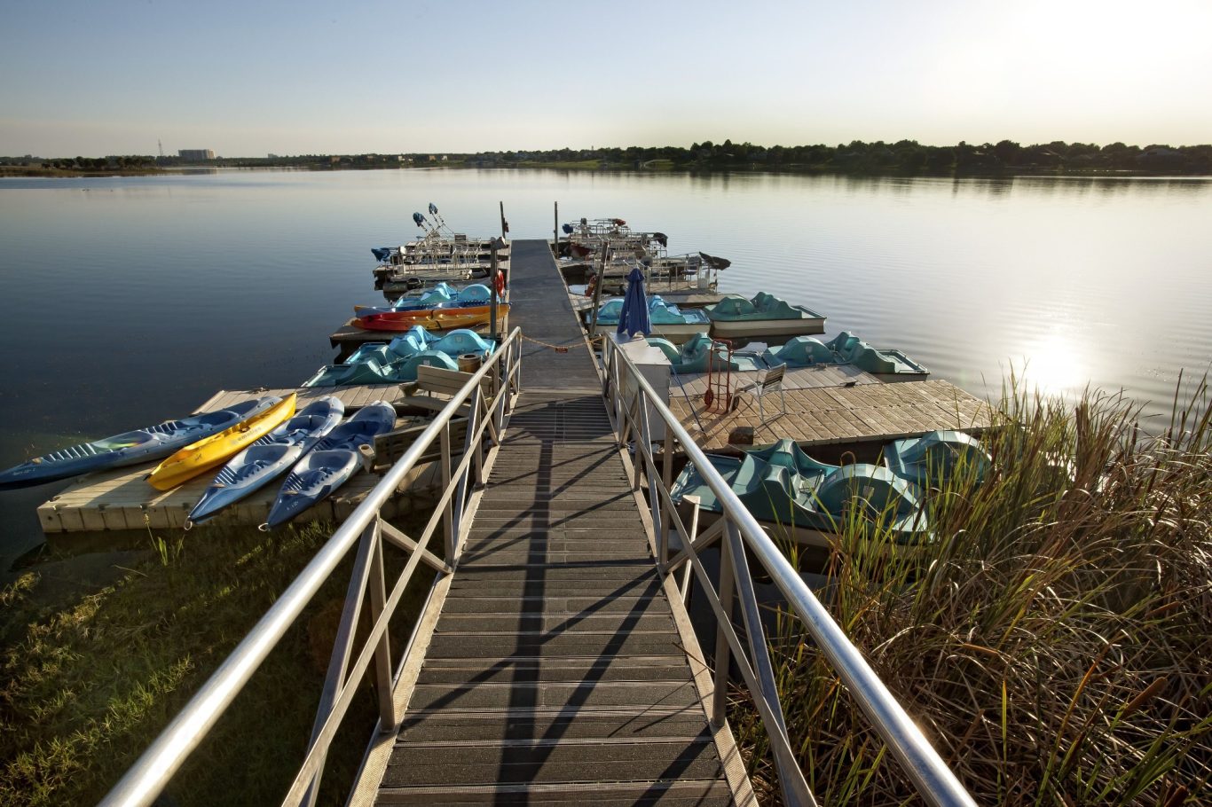A wooden dock extends over calm water, lined with colourful paddle boats.