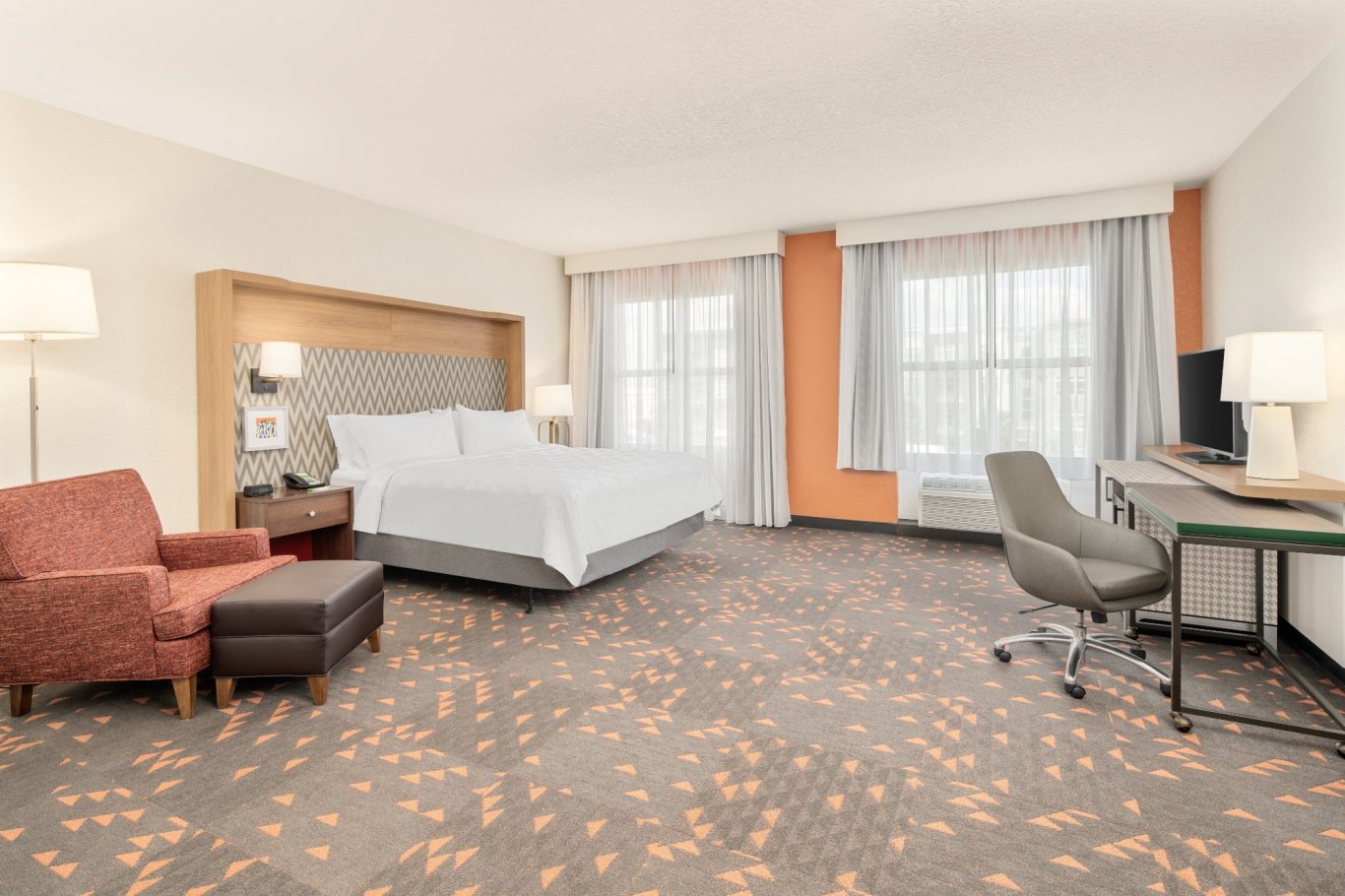 Modern hotel room featuring a king bed, desk, chair, and seating area.