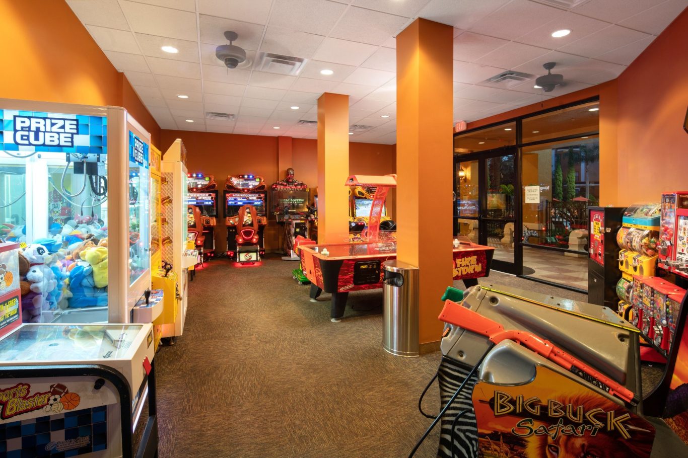 Bright arcade with various gaming machines and red tables in a warm-toned room.