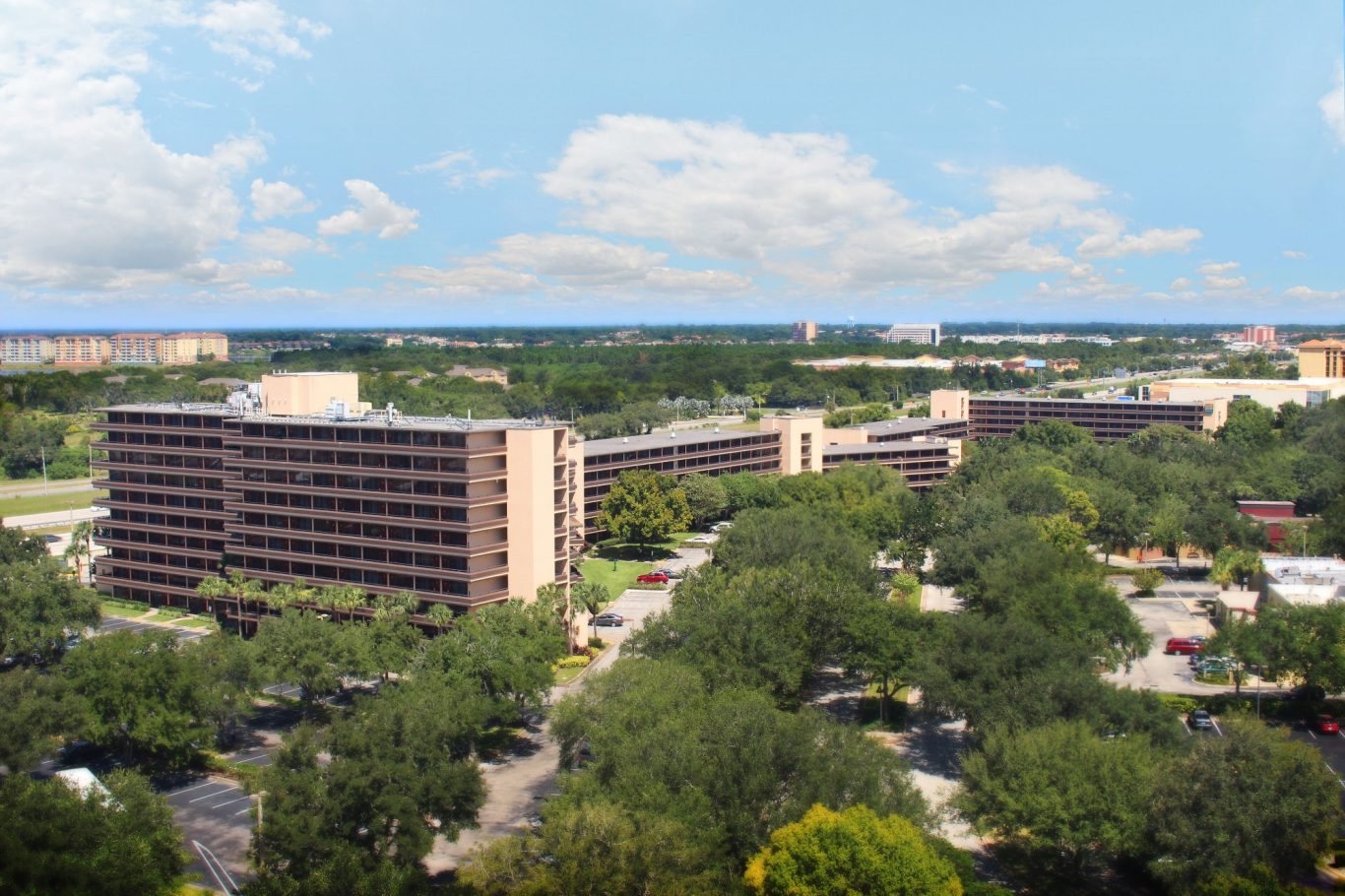 Aerial view of several low-rise buildings surrounded by green trees and blue sky.