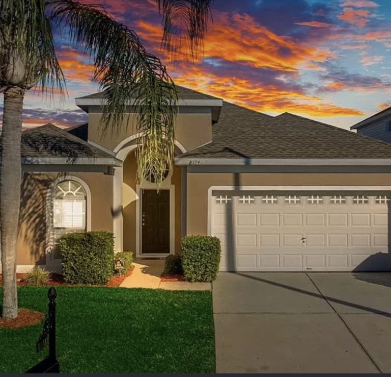 A modern house with a curved entrance and a three-car garage against a vibrant sunset.