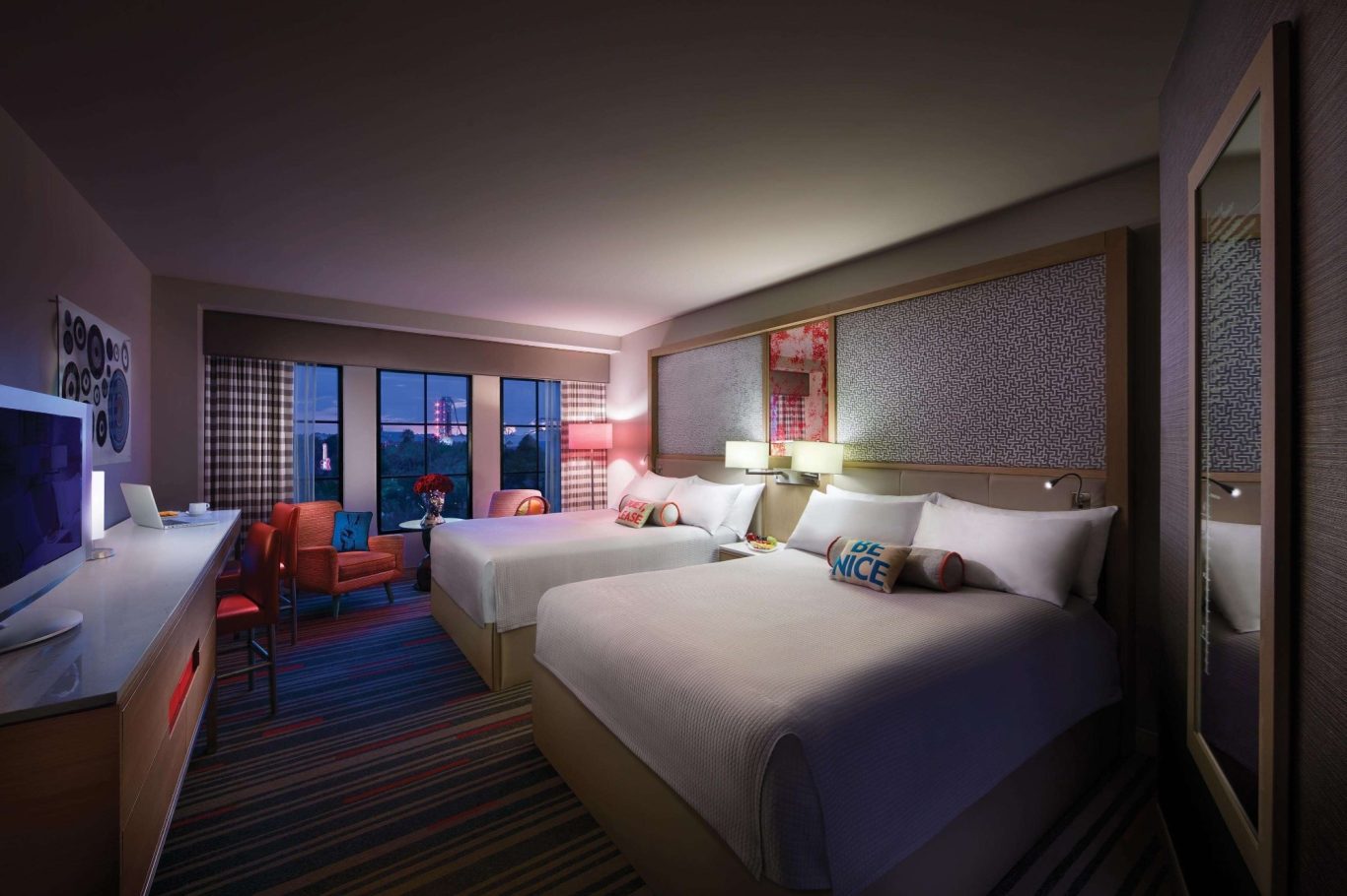 Bright hotel room with two beds, modern decor, and large windows showing a city view.