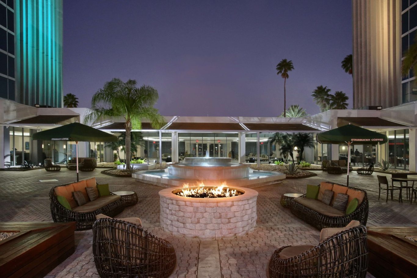 Outdoor lounge area with a fire pit, palm trees, and comfortable seating at dusk.