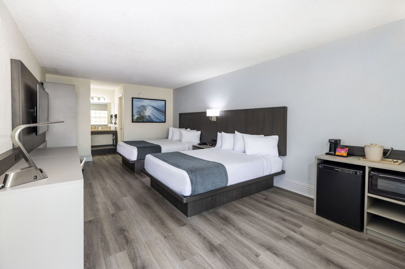 Hotel room with two double beds, a television, and a small kitchenette area.